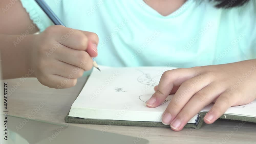 Child girl in blue shirt sitting and writing on blank notebook. Hand of little kid female drawing with pen on paper. Education learning people concept. Child girl in blue shirt sitting and writing on blank notebook. Hand of little kid female drawing with pen on paper. Education learning people concept.