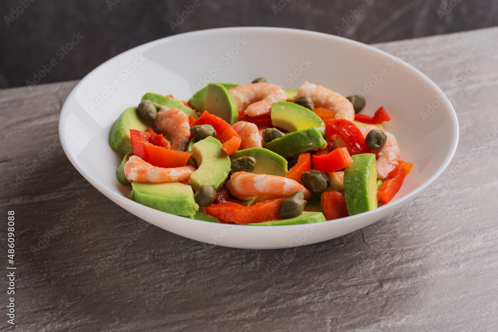 Salad with avocado, pepper, shrimps, capers on white plate. Mediterranean cuisine. Healthy food. Isometric style.