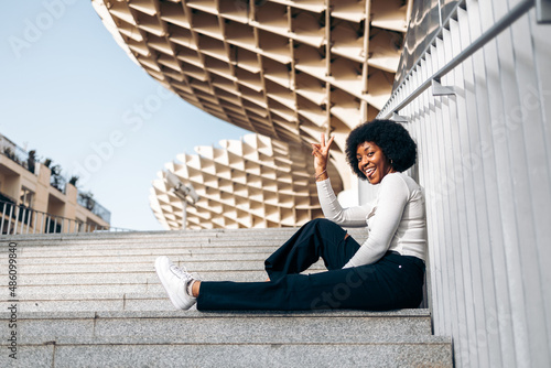 Beautiful black teenage girl making victory gesture sitting on some steps in the street