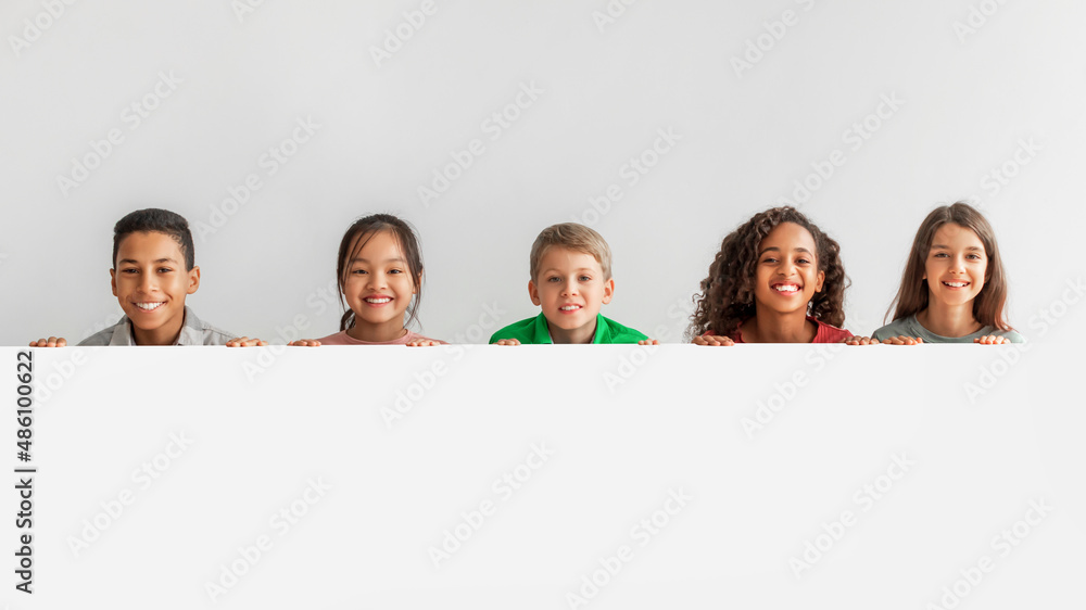 Happy Multicultural Children Posing With Empty White Poster, Gray Background Happy Multicultural Children Posing With Empty White Poster, Gray Background