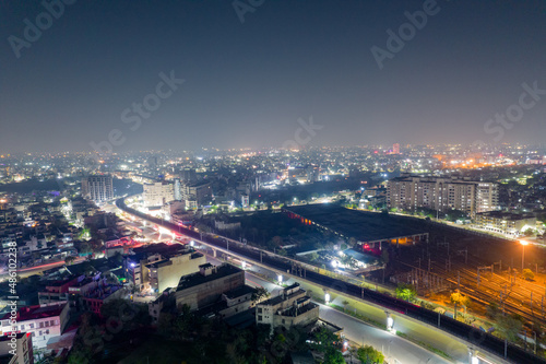 aerial drone shot showing elevated metro train station and tracks over busy street with light trails from traffic and cityscape in gurgaon, jaipur India