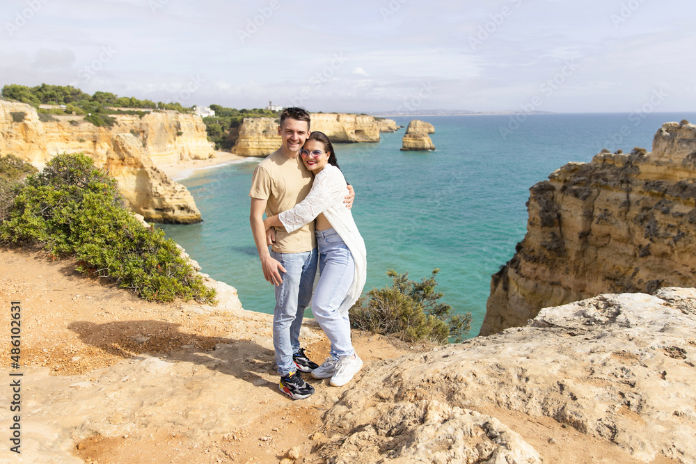 young beautiful couple stands on a rock against the backdrop of the beach and ocean beach in Portuga