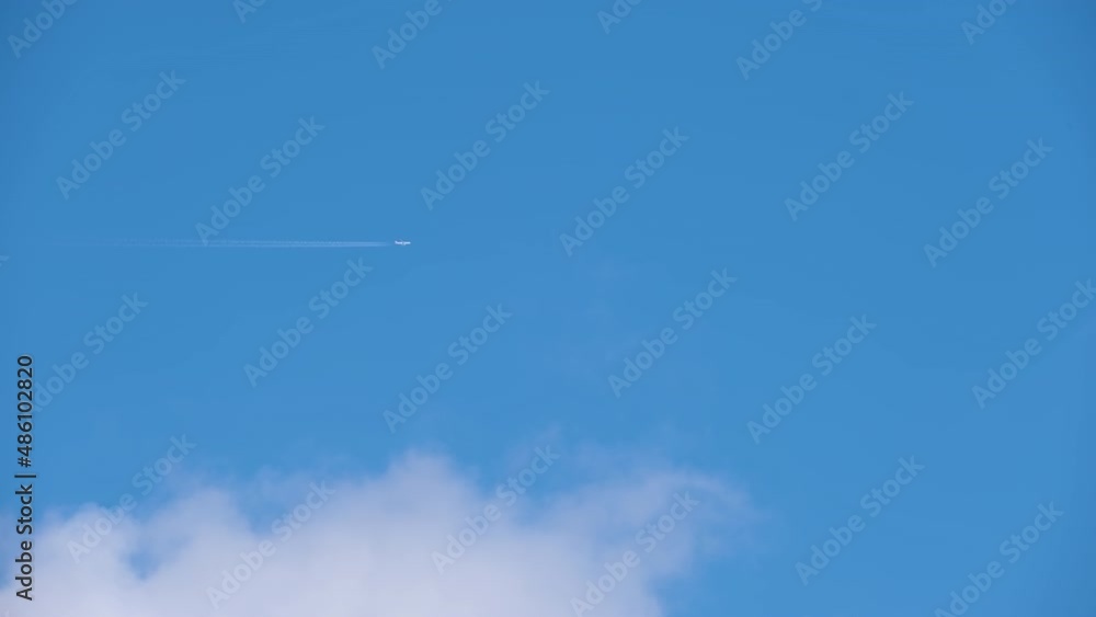 Distant passenger jet plane flying on high altitude on blue sky with white clouds leaving smoke trace of contrail behind. Air traveling concept Distant passenger jet plane flying on high altitude on blue sky with white clouds leaving smoke trace of contrail behind. Air traveling concept