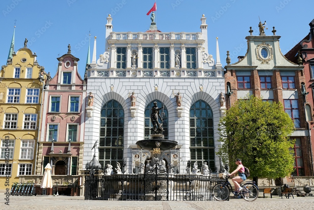 Naklejka premium Old Town and Neptune's Fountain in beautiful summer scenery, Gdansk, Poland. Blurry silhouette of a cycling woman in motion.