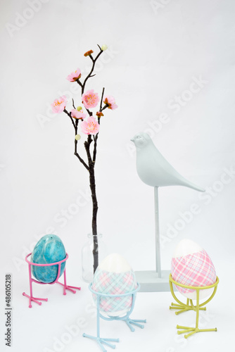 Moscow, Russia, February 2022, spring Easter still life, a figurine of a bird, a sakura branch in a jar and three Easter eggs with bird legs on a white background © Iuliia