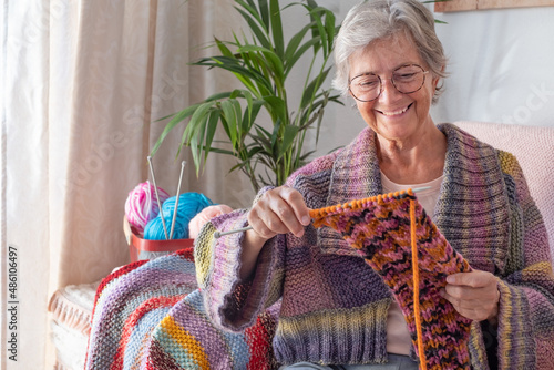 Foto Senior smiling woman sitting on sofa at home while knitting and looking at her work in progress