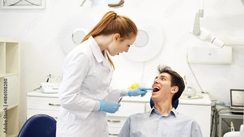Young friendly female dentist talking with male patient sitting in chair about oral health hygiene Young friendly female dentist talking with male patient sitting in chair about oral health hygiene