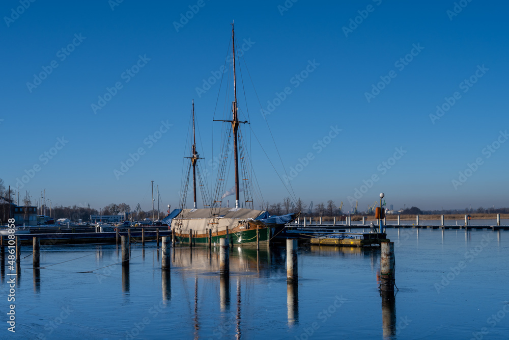 A sailboat in a marina closed down for winter. Blue water and a clear blue sky
