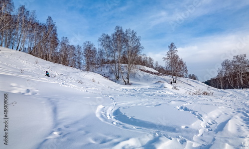 Winter landscape with birch trees on the mountain bank of the river, snow and blue sky with clouds