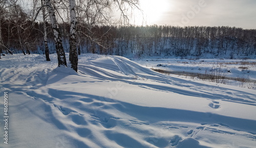 Winter landscape with birches, river, snow and blue sky with clouds