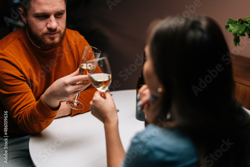 Close-up high-angle view of young couple clinking glasses of wine sitting at table with candles in dark cozy room. Loving man and woman celebrating anniversary, Valentines day, enjoying romantic date.
