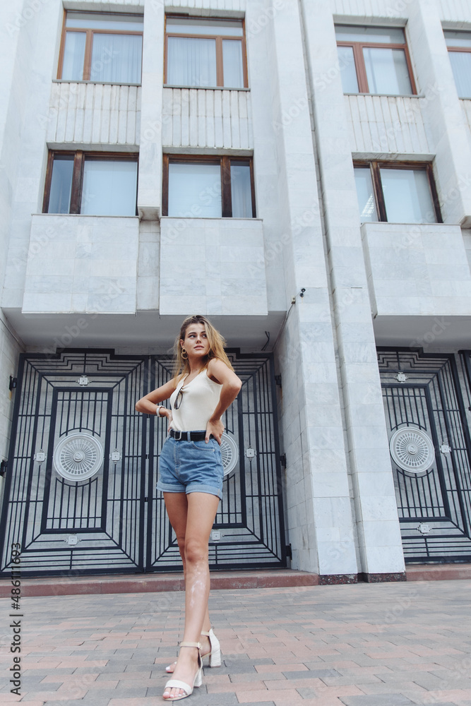 Stylish vertical urban portrait of a young woman against the backdrop of a tall building. Woman Teenager Portrait Hipster Style Concept