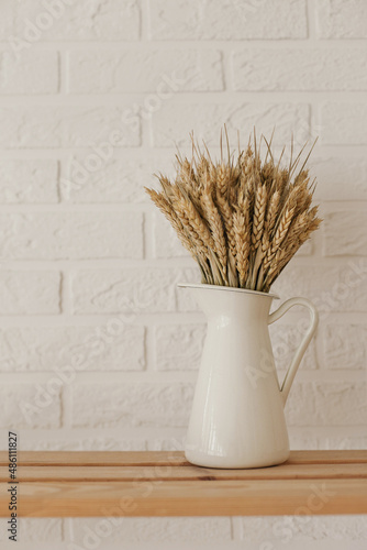 A bouquet of dry wheat in white jug vase on the shelf at home with white brick wall as background. MJinimalist apartment background with copy space on the left and top.