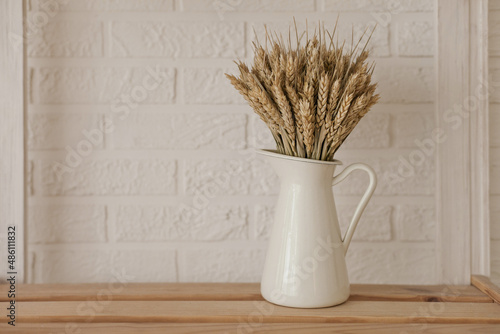 A bouquet of dry wheat in white jug vase on the shelf at home with white brick wall as background. MJinimalist apartment background with copy space on the left.