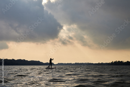 Silhouette of sportswoman standing on paddle board on river with stormy cloudy sky