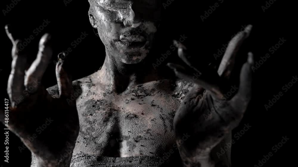 alluring woman is covered by clay and with blindfold is moving hands and fingers to camera alluring woman is covered by clay and with blindfold is moving hands and fingers to camera