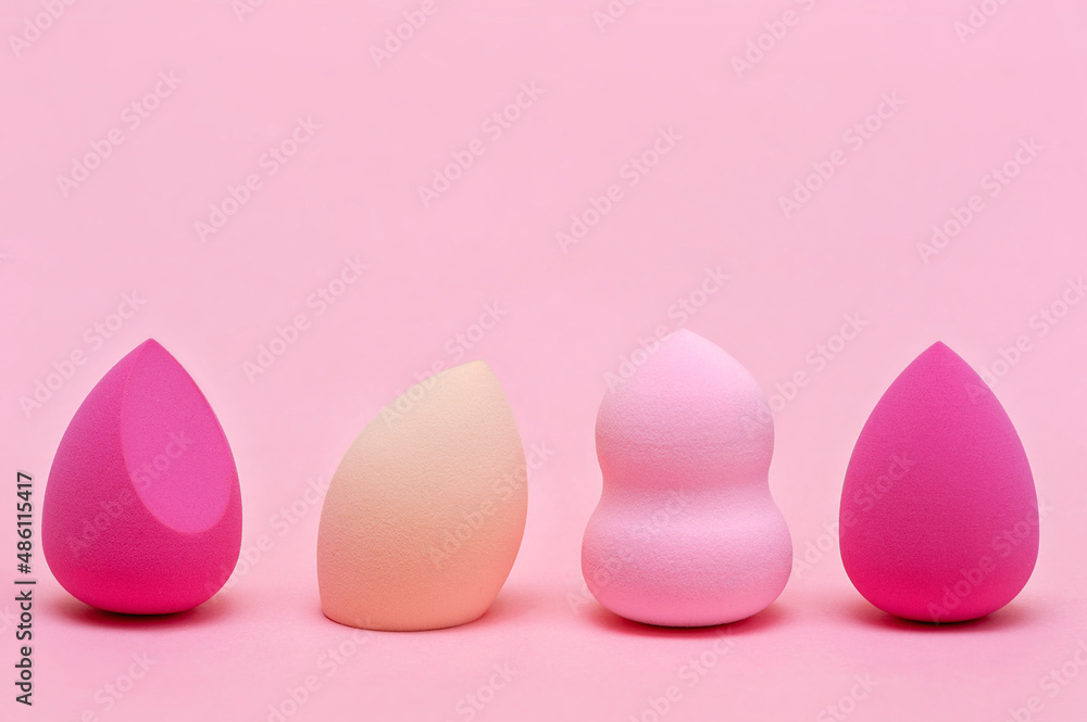 Makeup sponges of different colors and different shapes on a pink background
