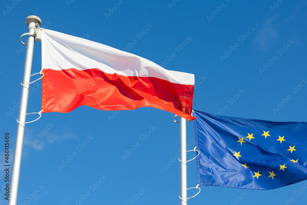 The flags of Poland and the European Union waving against the blue sky