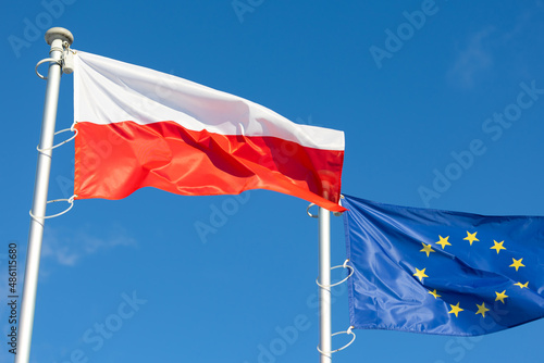 The flags of Poland and the European Union waving against the blue sky