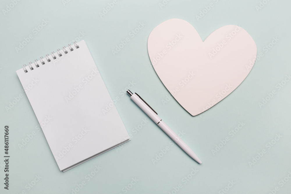 Top view of open spiral blank notebook with pen and white paper heart on white desk background. Isolated on mint color backdrop. Top view of open spiral blank notebook with pen and white paper heart on white desk background. Isolated on mint color backdrop.
