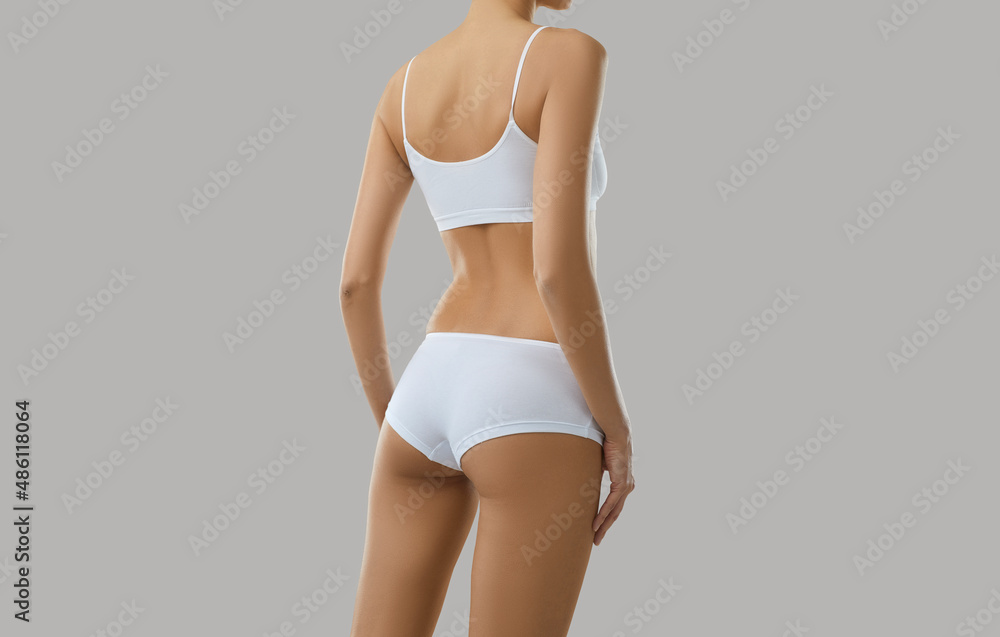 Fototapeta premium Crop rear view of toned sexy female model in underwear isolated on grey studio background. Slim woman back butts in organic cotton underclothing wear or pajama advertise good quality home garment.