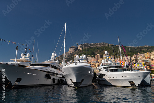 A lot of huge yachts are in port of Monaco at sunny day, Monte Carlo, mountain is on background, glossy board of the motor boat, megayachts are moored in marina, sun reflection on glossy board