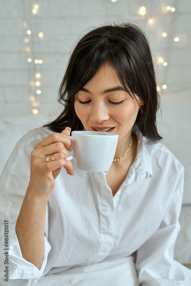 Portrait of a brunette girl with a cup of tea on the bed. Portrait of a brunette girl with a cup of tea on the bed.