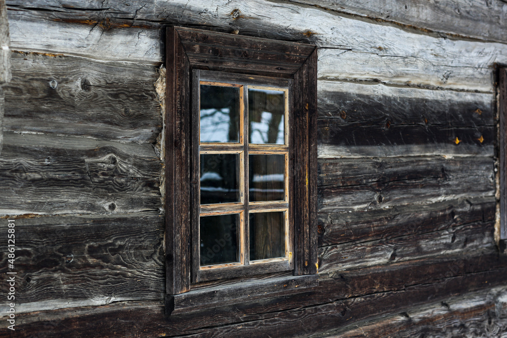 Rustic wooden house made of round logs. Abandoned villages and houses. Ancient window design. Wooden window frame. Snow covered village. Age-old buildings. Professional photography.