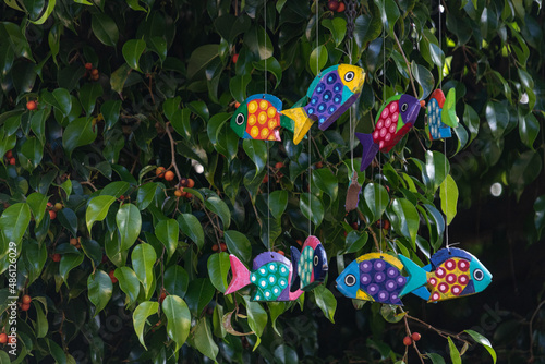Colorful cheerful painted fish mobile hanging in a tree with red berries, spring and summer fun