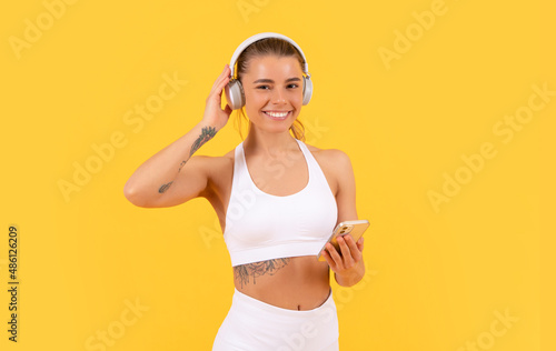 happy sport woman with headphones and smartphone on yellow background