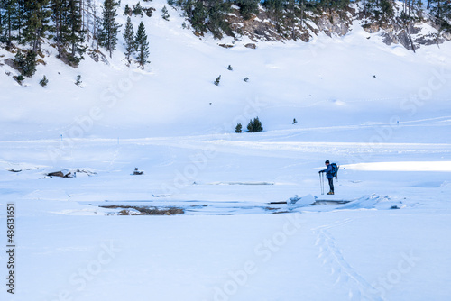 Man standing in the middle of a snowy valley on the edge of a frozen lake. Ski. Mountaineering. Snow shoeing. Winter sports in the Pyrenees. Snow landscape.