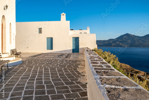 Greece, Milos island, Chora town, Plaka. White building and stone paved yard over calm sea, Cyclades