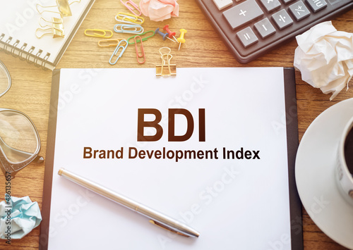 BDI acronym for brand development index. Text on white sheet of paper and office accessories on wooden desk. photo