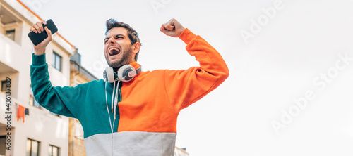 man with phone and headphones in the street excited with joy celebrating success