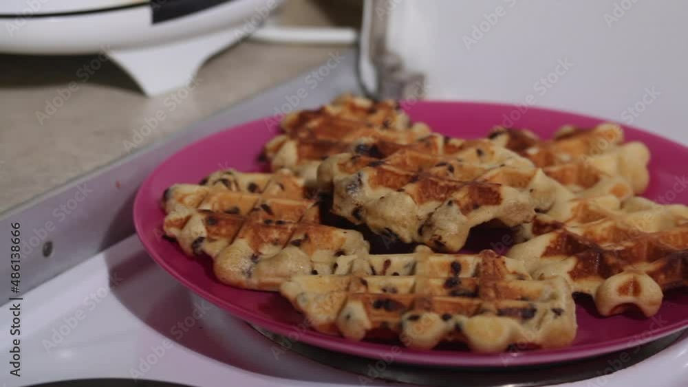 A woman checks the readiness of waffles in an electric waffle iron. Freshly made waffles on a plate. Breakfast preparation. Close-up. A woman checks the readiness of waffles in an electric waffle iron. Freshly made waffles on a plate. Breakfast preparation. Close-up.