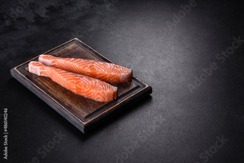 Fresh salmon fillets on black cutting board with herbs and spices