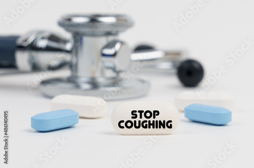 On a white surface lie pills, a stethoscope and a tablet with the inscription - STOP COUGHING