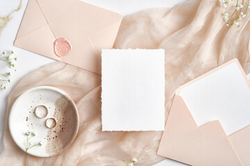 Wedding invitation card mockup, wedding envelopes, rings on beige cloth. Flat lay, top view.