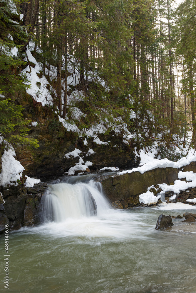 Small waterfall  in winter mountain forest in snow