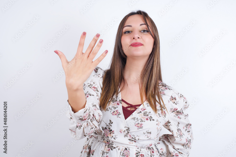 young Arab woman wearing floral dress over white background smiling and looking friendly, showing number five or fifth with hand forward, counting down young Arab woman wearing floral dress over white background smiling and looking friendly, showing number five or fifth with hand forward, counting down