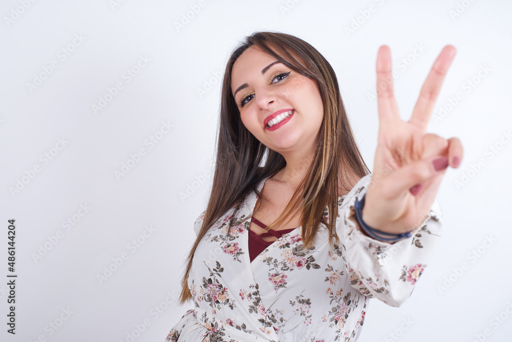young Arab woman wearing floral dress over white background directs fingers at camera selects someone. I recommend you. Best choice young Arab woman wearing floral dress over white background directs fingers at camera selects someone. I recommend you. Best choice