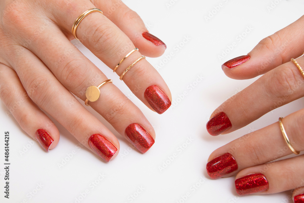 Manicure gel polish of red color with sparkles on female hands with rings. Top view Manicure gel polish of red color with sparkles on female hands with rings. Top view
