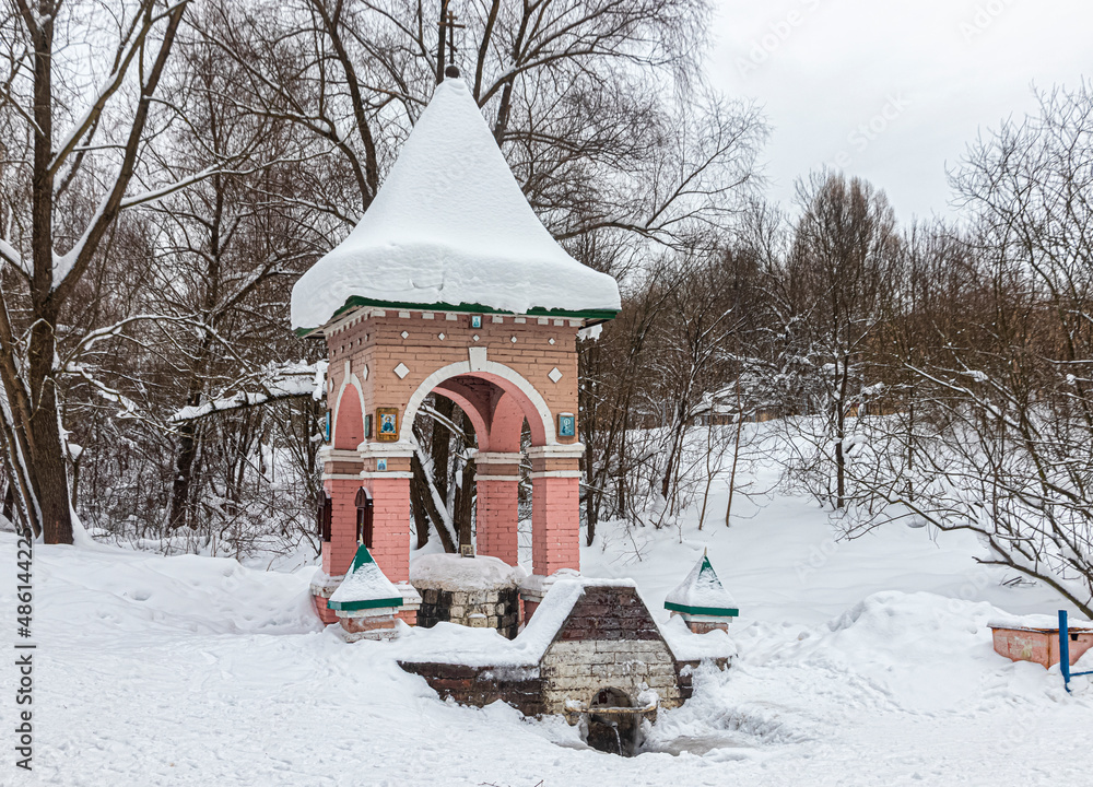 Naklejka premium Chapel with a snow-covered dome, near a spring, in a wooded area