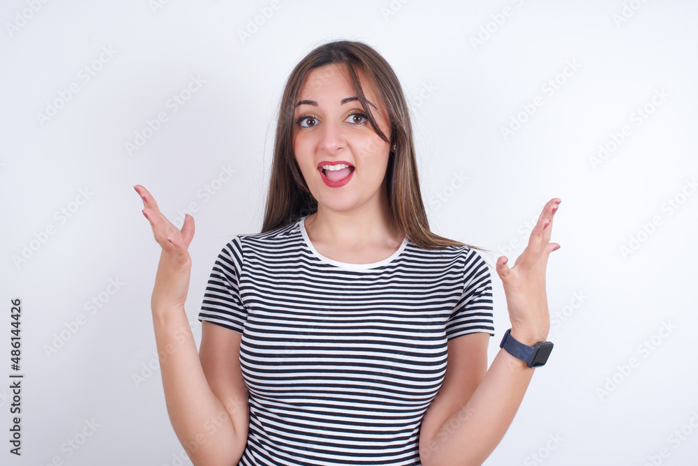 Crazy outraged young Arab woman wearing striped t-shirt over white background screams loudly and gestures angrily yells furiously. Negative human emotions feelings concept Crazy outraged young Arab woman wearing striped t-shirt over white background screams loudly and gestures angrily yells furiously. Negative human emotions feelings concept