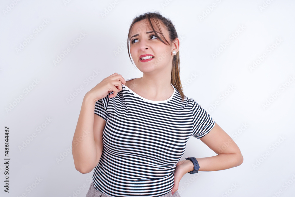 young Arab woman wearing striped t-shirt over white background stressed, anxious, tired and frustrated, pulling shirt neck, looking frustrated with problem young Arab woman wearing striped t-shirt over white background stressed, anxious, tired and frustrated, pulling shirt neck, looking frustrated with problem
