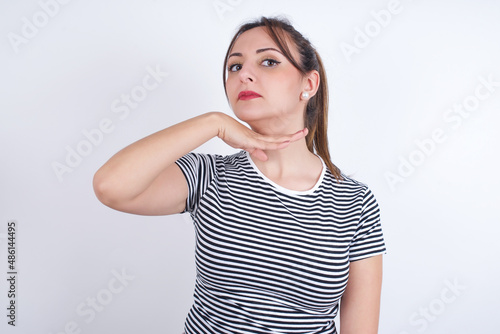 young Arab woman wearing striped t-shirt over white background cutting throat with hand as knife, threaten aggression with furious violence. photo
