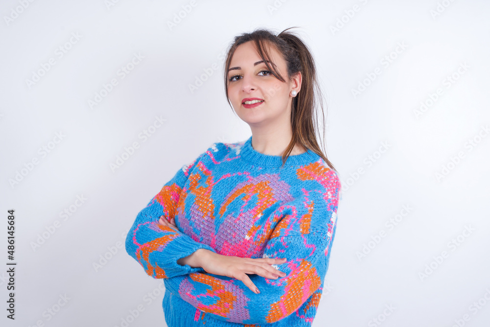 Portrait of young arab woman wearing knitted sweater and ponytail over white background standing with folded arms and smiling Portrait of young arab woman wearing knitted sweater and ponytail over white background standing with folded arms and smiling