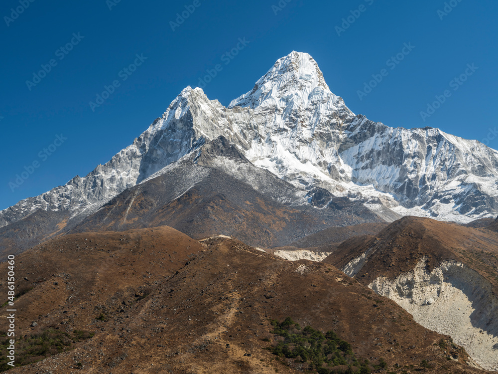 view to mount Ama-Dablam through brown hills in summer day under blue sky in Nepal