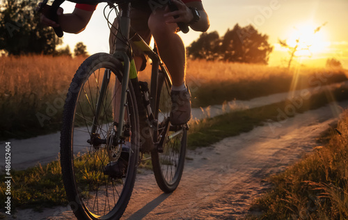 Cyclist rides a bicycle on the countryside dirt road at sunset. Athletic guy on a gravel bike training on fresh air.