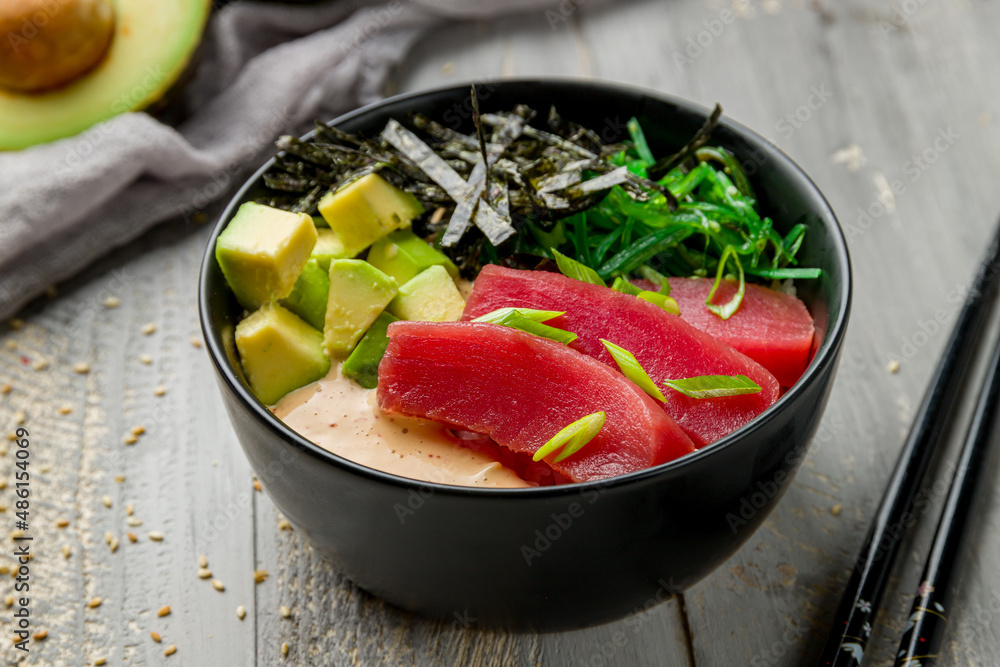 Ahi poke with tuna, avocado, chukka and sauce with rice on black bowl on grey wooden table macro close up Ahi poke with tuna, avocado, chukka and sauce with rice on black bowl on grey wooden table macro close up